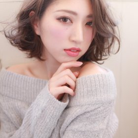 顎に手を置くアッシュブラウンのボブスタイルの女性の写真