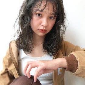 強めのパーマをかけて髪留めをつけたロングヘアの女性の写真