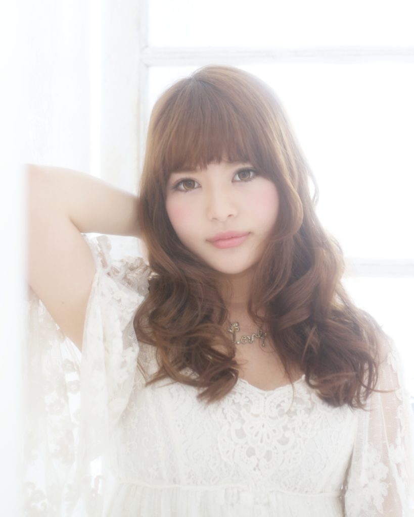 前髪ありのロングパーマヘアの白いブラウスを着た女性の写真