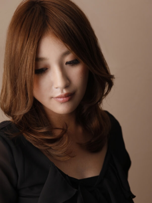 少しうつむく、センター分けでゆるくウェーブがかったミディアムヘアの女性の写真
