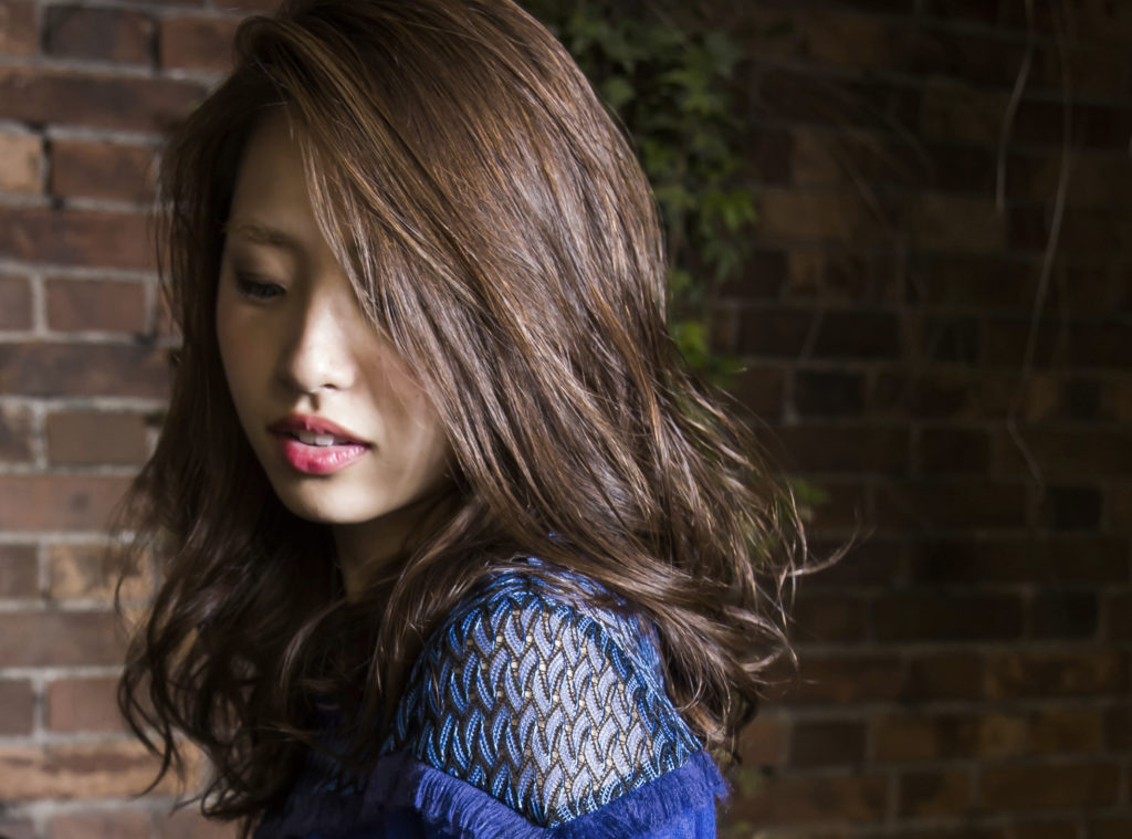 前髪セパレートの明るいブラウンロングヘアの斜め下を向いた女性の写真