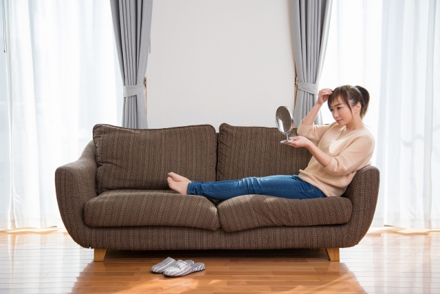 ソファに座って鏡で髪の毛を見る女性の写真