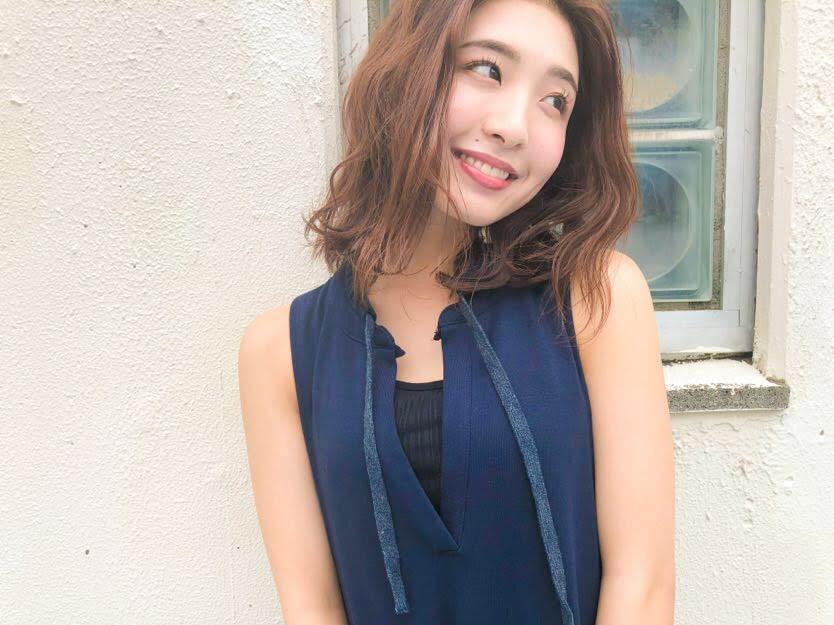 白い壁の前に立つウェーブヘアの女性・イーエムエーのスタイル写真