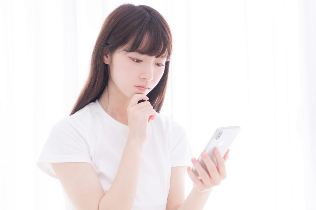スマホを見て考える女性の写真