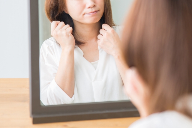 ミドルヘアの女性が髪を触りながら微笑む姿を鏡に映したイメージ