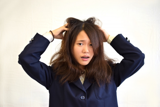 上着を着た女性がくせ毛に悩み髪をかき上げる様子