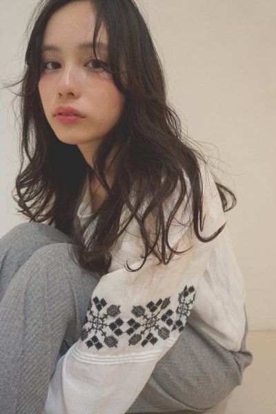 自然にウェーブするロングヘアの柄もののセーターを着た女性の写真