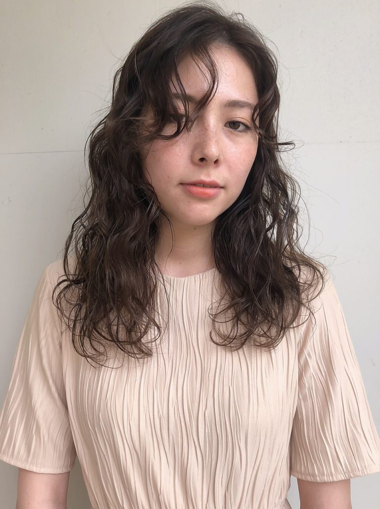 ナチュラルメイクのウェーブヘア女性がはにかむ様子