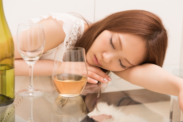 アラサーの女性がお酒を飲んでテーブルでうたた寝する様子