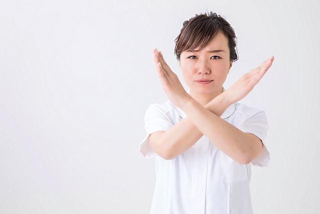 手でバツを作る白衣の女性