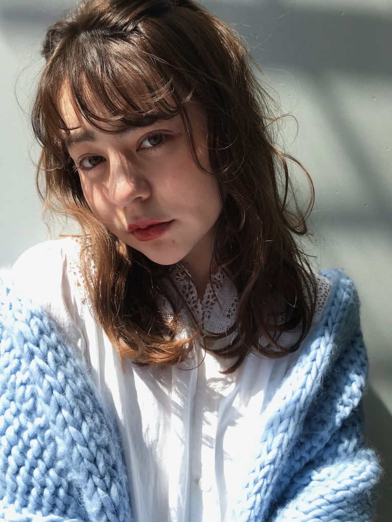 水色のセーターを羽織ったナチュラルウェーブミディアムヘアの女性