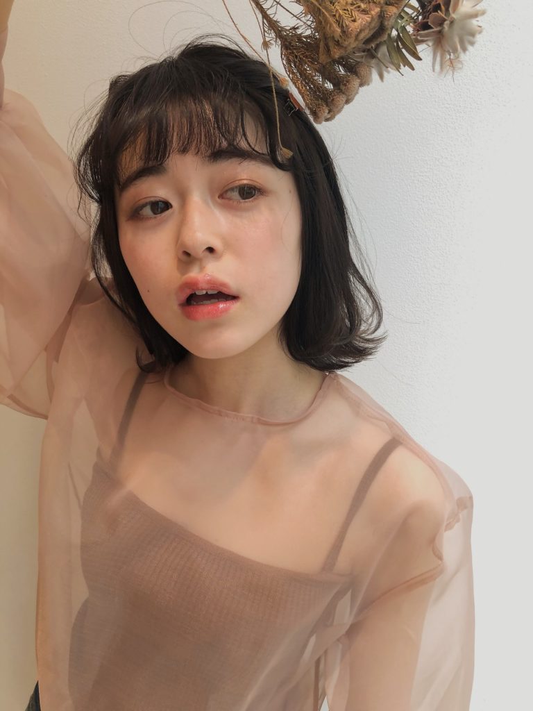右手を上げてポーズをとる長めのボブヘア女性