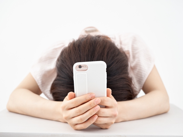 電話を持ちながら悩みうつむく女性の様子