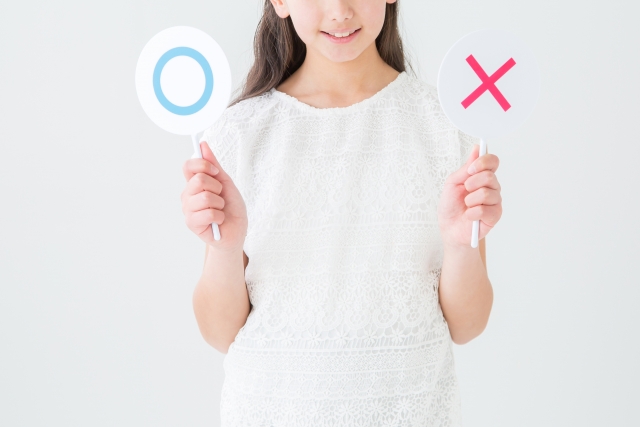 丸とバツの札を持って笑う女性
