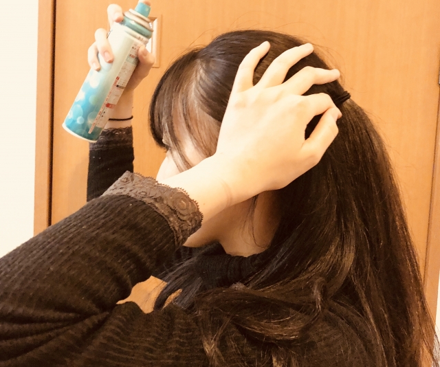 髪にスプレーを噴射する女性