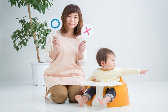 丸とバツの札を持って笑う幼い子を持つ女性