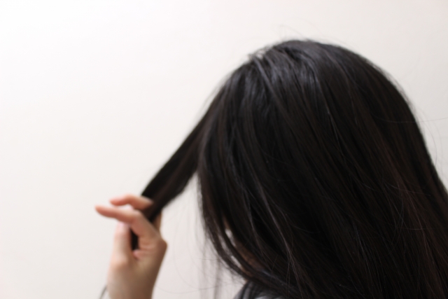 手ぐしで髪を梳かす若い女性の後ろ姿