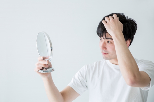 頭皮を鏡で見ている白シャツの男性