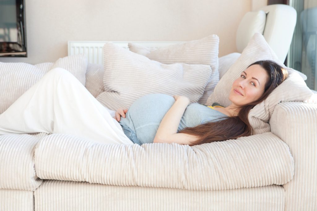 ソファーに寝そべる妊婦の写真