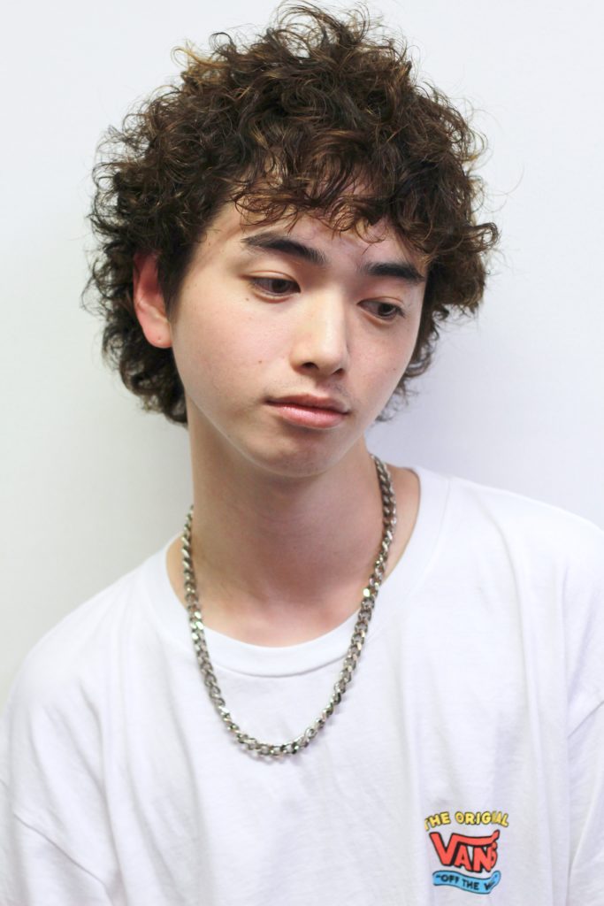 手を口に添えているメンズショートパーマスタイルの男性の写真