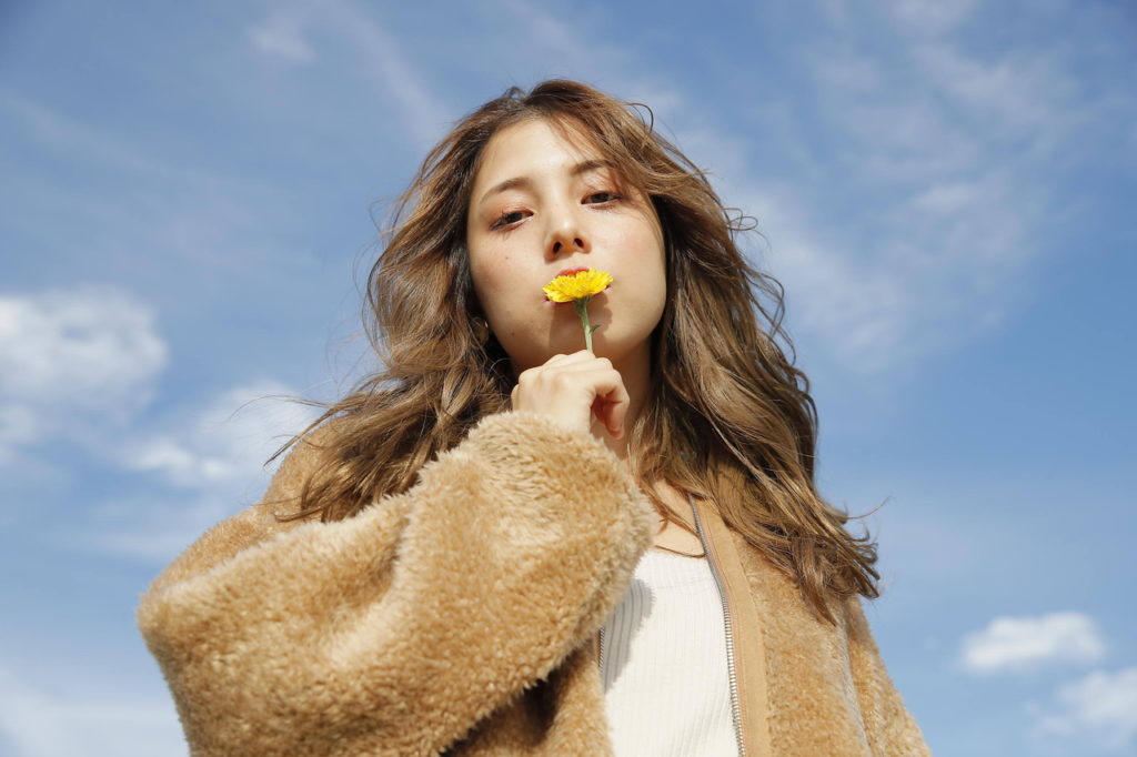 青空をバックに花を持つ女性の写真