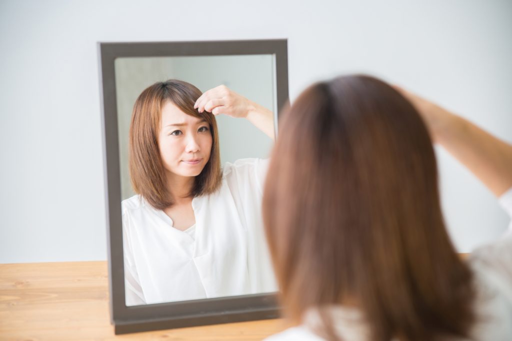 前髪を鏡でチェックする女性の写真