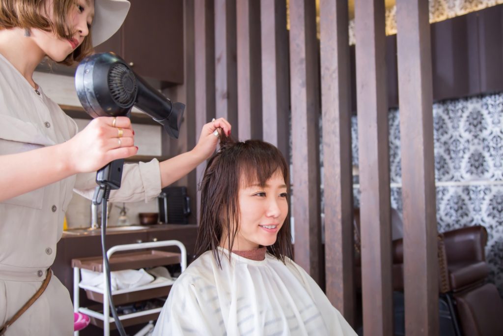 日本人美容師に髪を乾かしてもらっている女性の写真