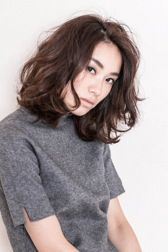 ふんわりかき上げた前髪がとても格好良いパーマヘアの女性の写真