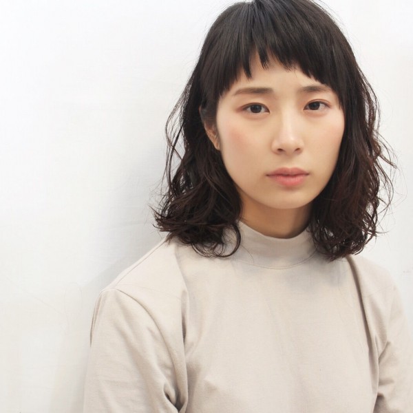 丸いラインにカットされた前髪が柔らかさをプラスする、ミディアムパーマヘアの女性の写真