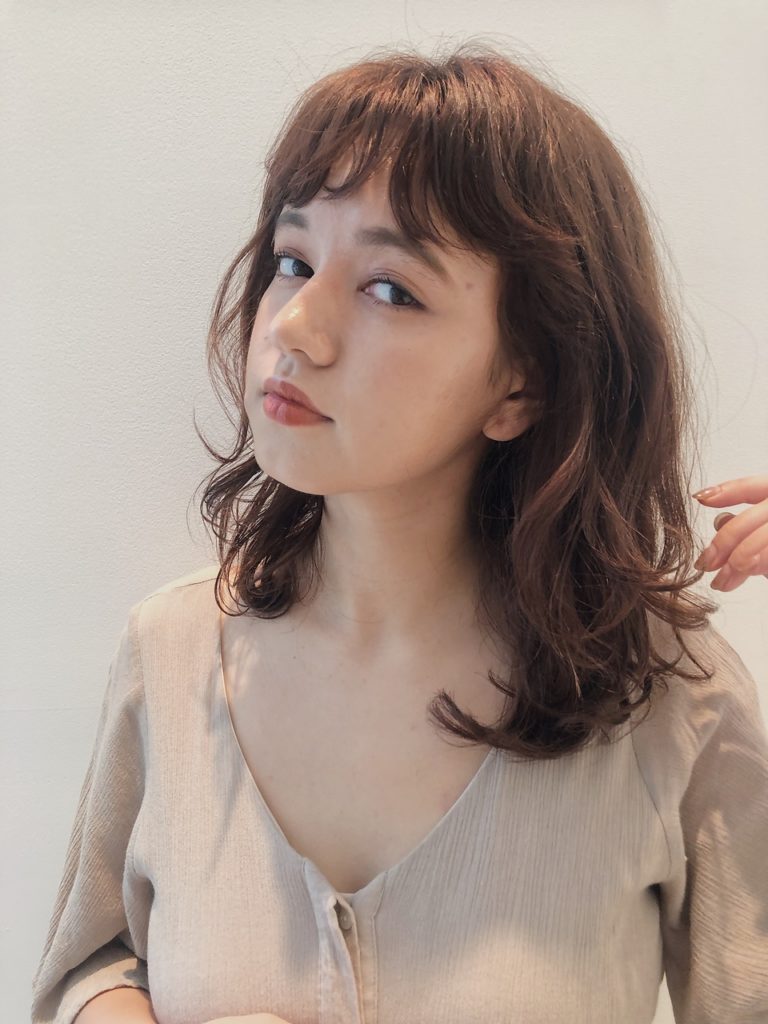 重めの短め前髪がオシャレなふんわりパーマヘアの女性の写真
