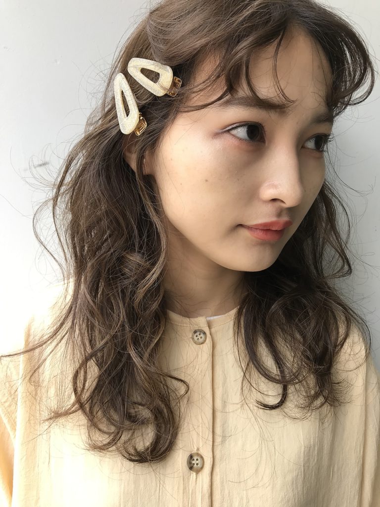 フワっとサンター分けした前髪の横側を、ヘアピンで留めてヘアアレンジをした女性の写真