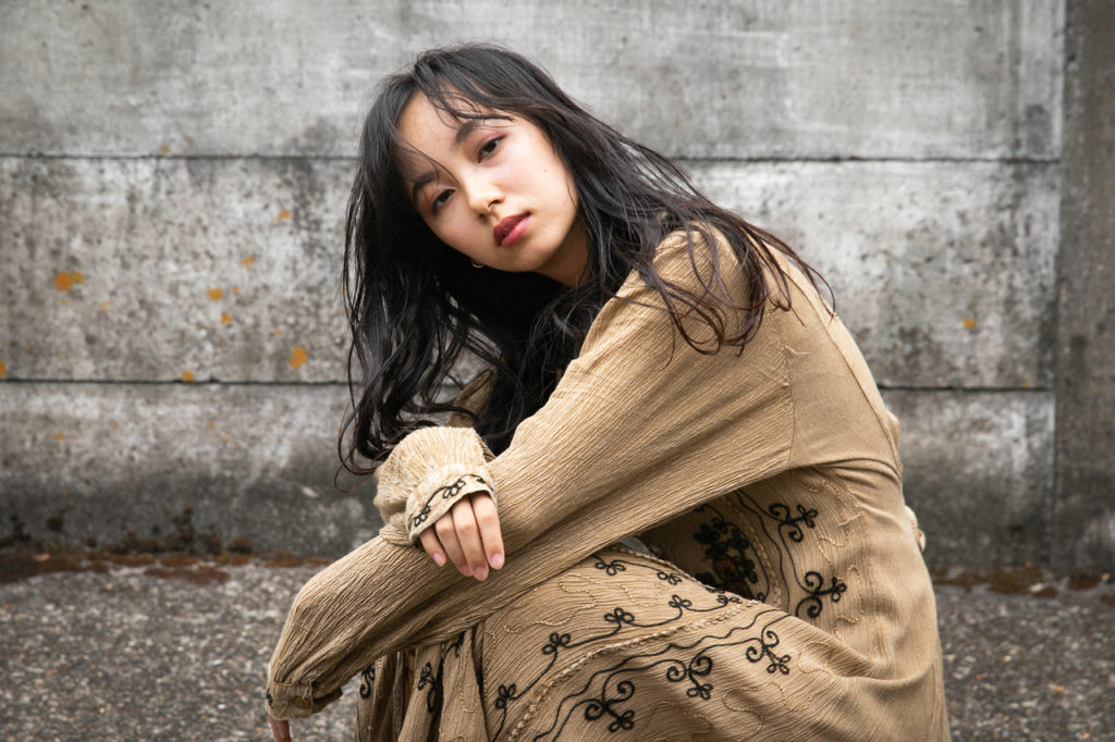 壁の前でしゃがんでいるサラサラウェーブヘアの女性の写真