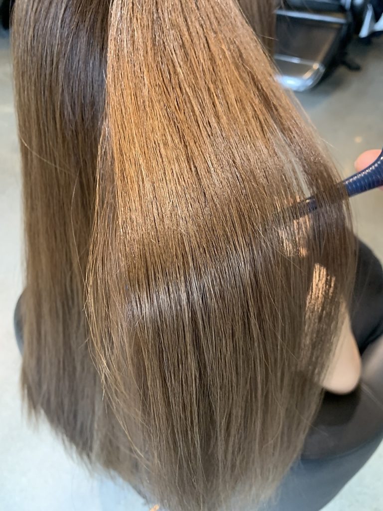 明るくヘアカラーしたツヤのある毛先をコームで持ち上げている写真