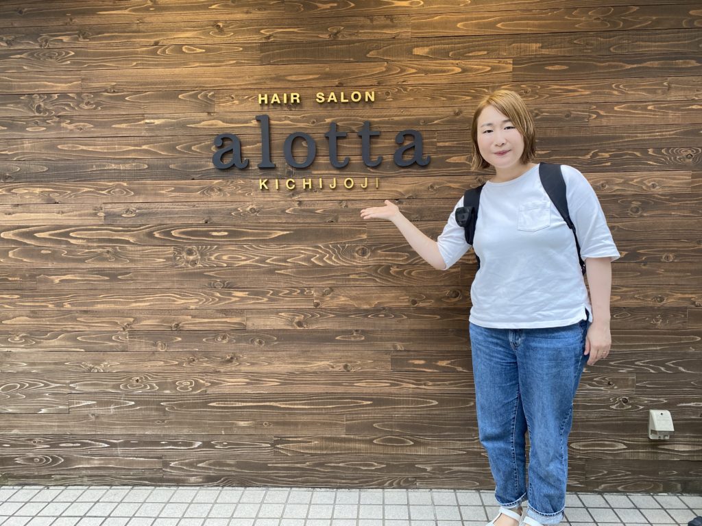 アロッタの看板の前に立ち紹介する女性の写真
