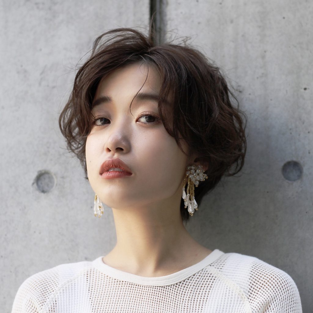 ゆるいウェーブのセンター分けをしたショートヘアの女性の写真