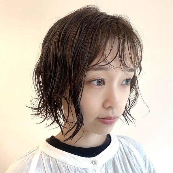 パーマをかけたショートスタイルの女性が口に手をあてている写真